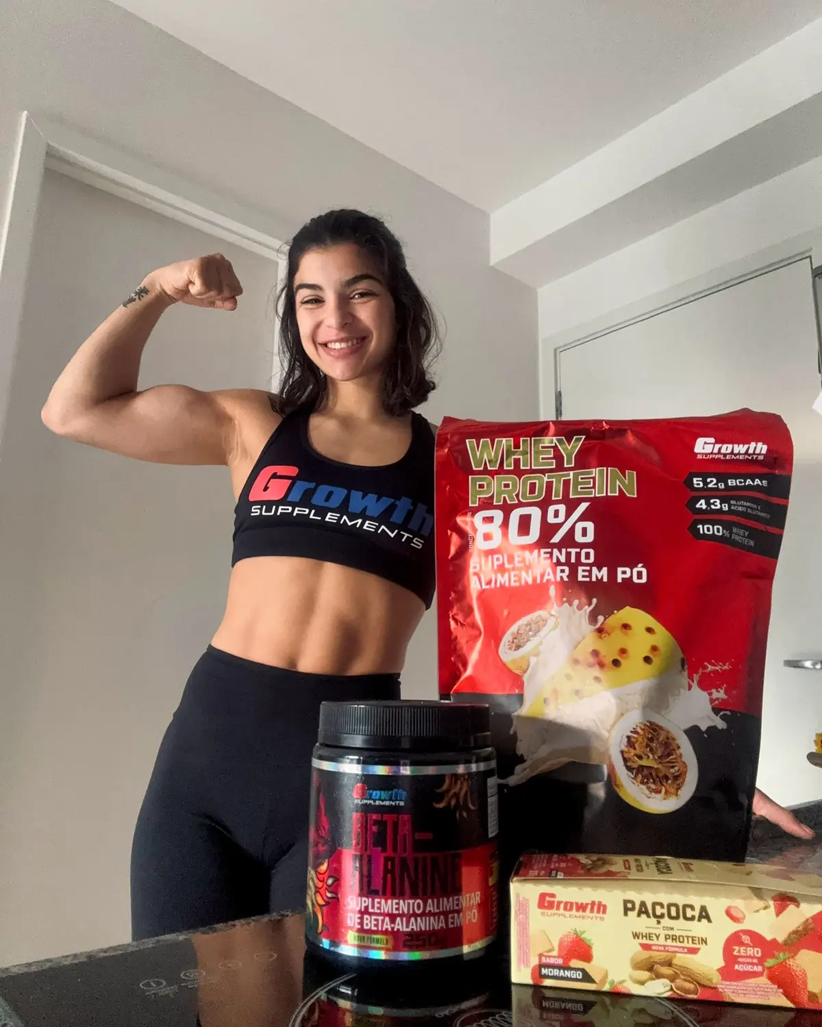 Foto real da Paula — braço forte + Whey Growth 80% maracujá + Paçoca